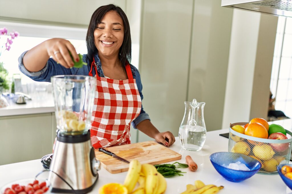 hispanic brunette woman preparing fruit smoothie at the kitchen
