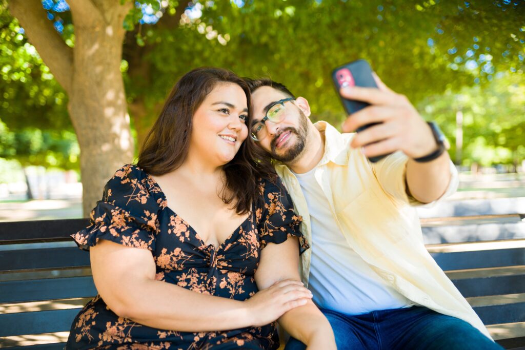 latin woman and caucasian man taking a selfie with a smartphone outdoors